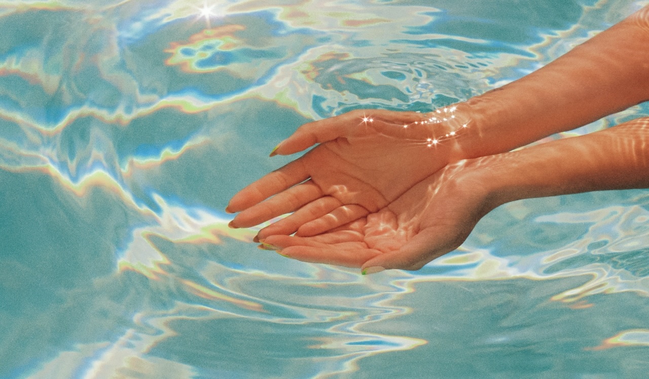 A pair of hands dipping into a clear body of water
